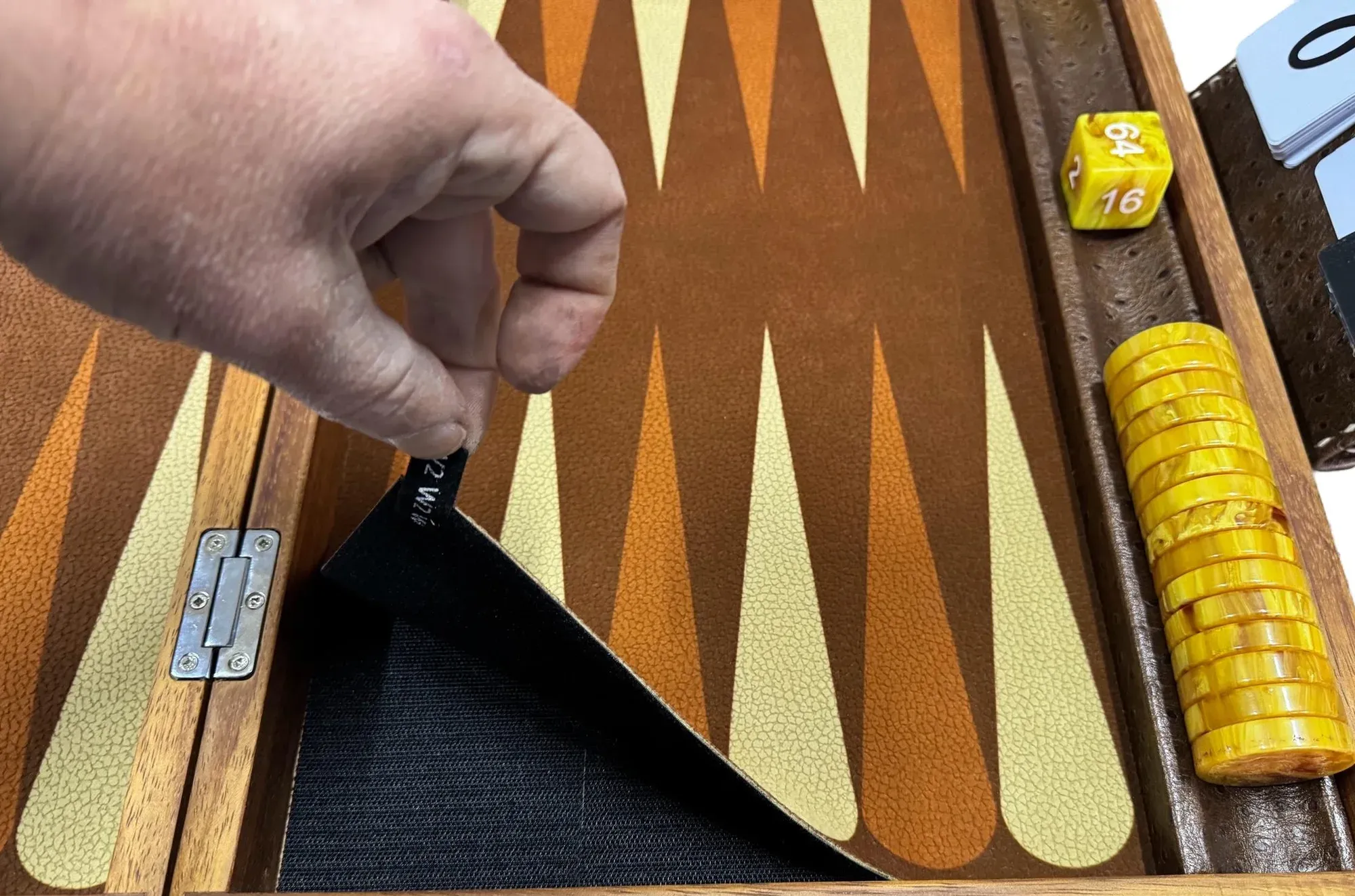 A hand lifting the replaceable playing surface out of a teak board